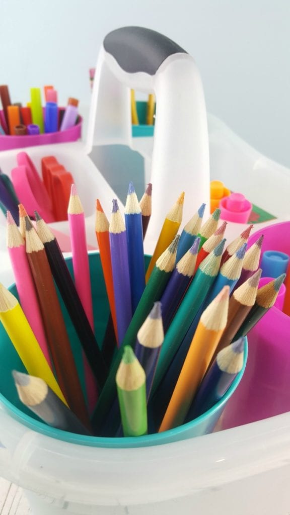 A close up of colored pencils in a clear plastic caddy with other school supplies.