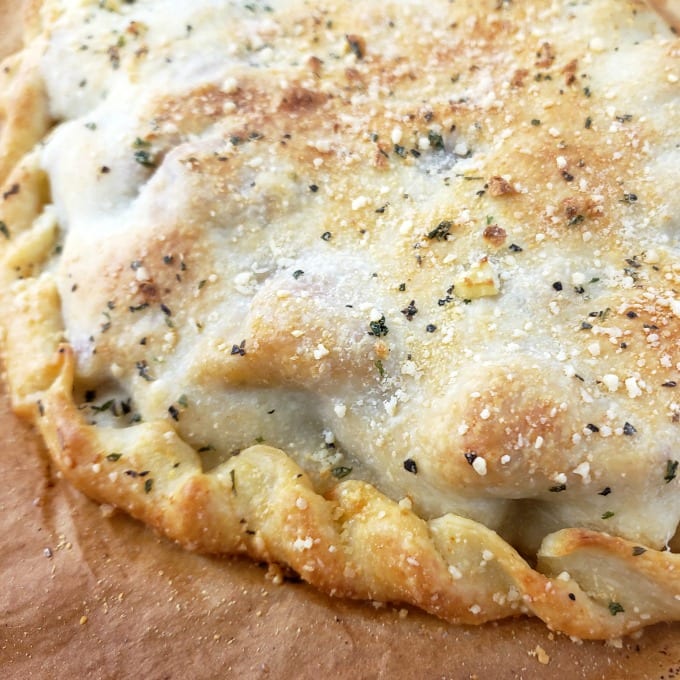A close up of a baked meatball calzone on parchment paper.