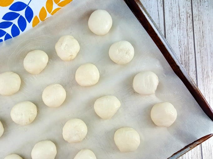 Frozen dinner roll dough on a parchment paper lined sheet pan.