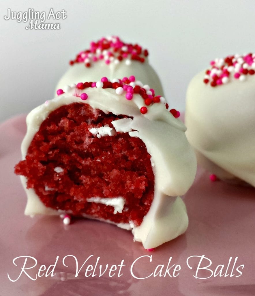 A red Velvet Cake Ball covered with white chocolate sits on a pink plate with a bite taken out of it