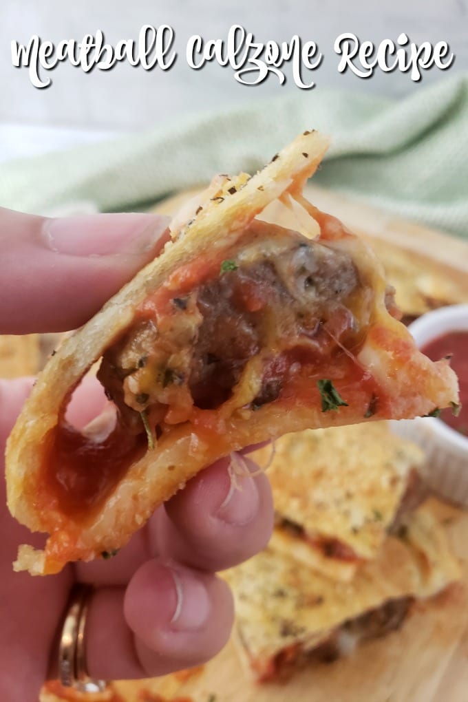 a close up of a hand holding a piece of meatball calzone