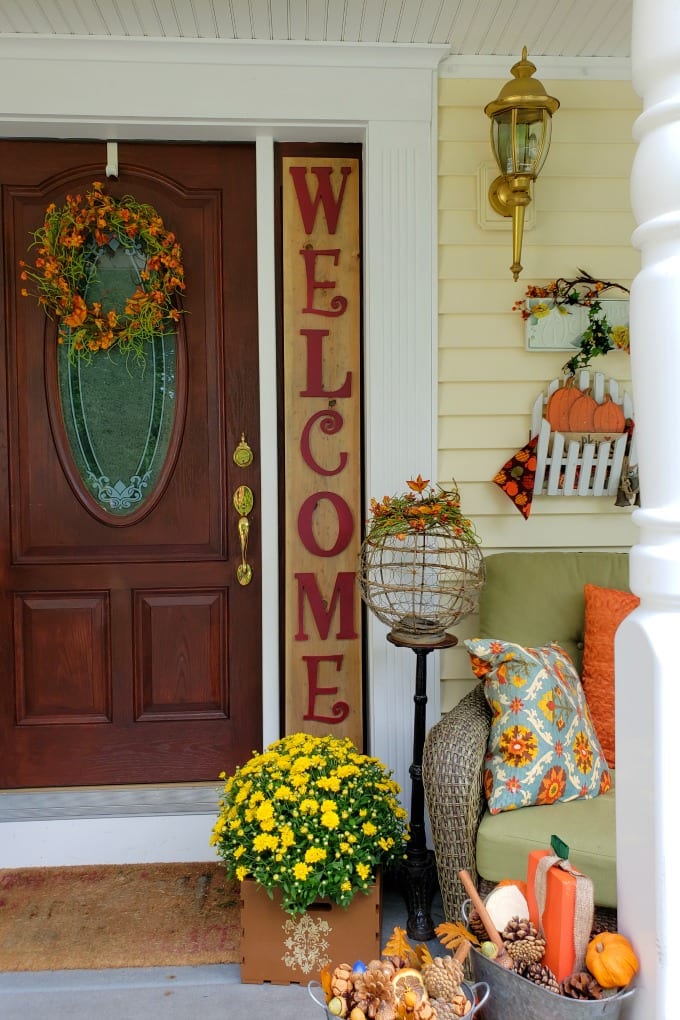 Fall porch decorated with welcome sign, mums and other seasonal decor.
