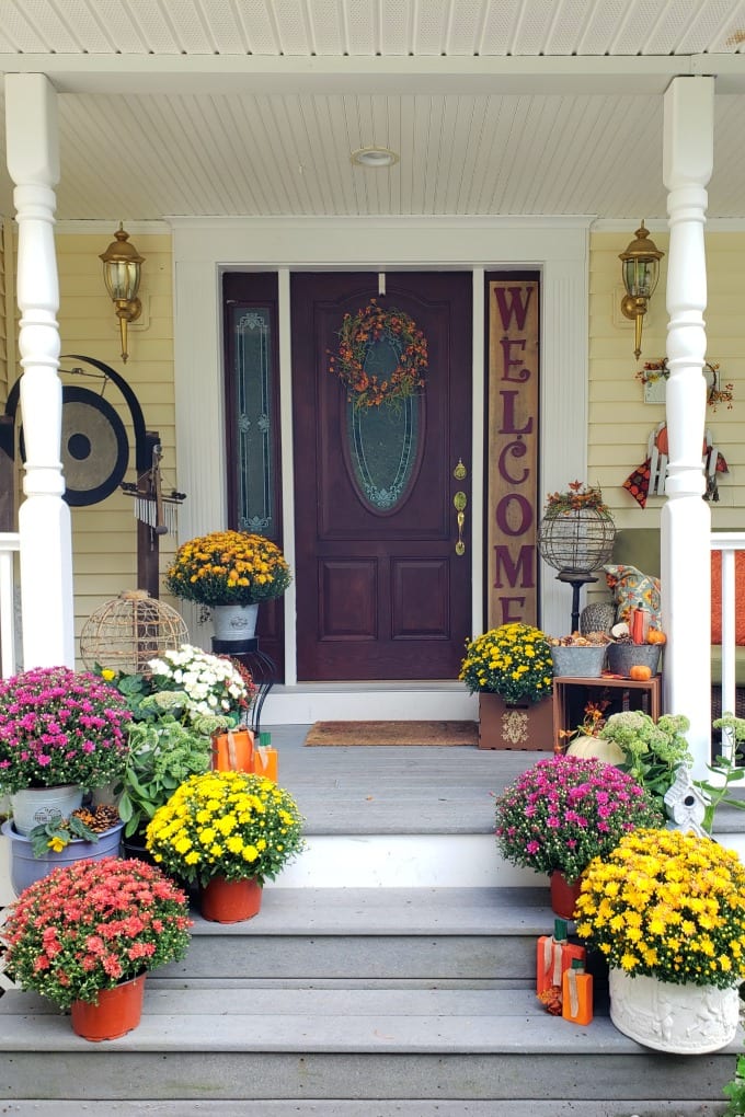 Fall Porch Decorating Ideas - a porch and front door decorated for Fall with colorful mums, pumpkins and other decorations.