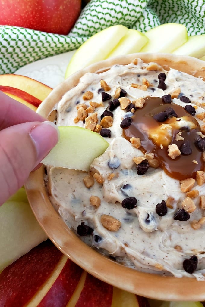 A hand holds an apple slice scooping up Toffee Apple Dip