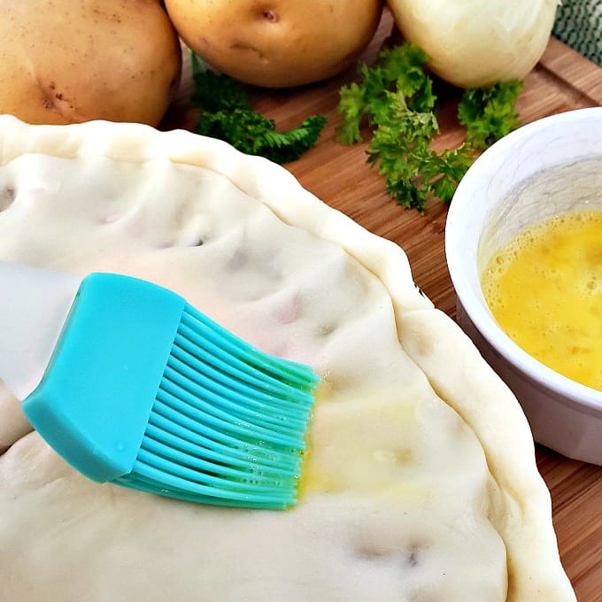 Close up of a pastry brush adding an egg wash to a pie crust.