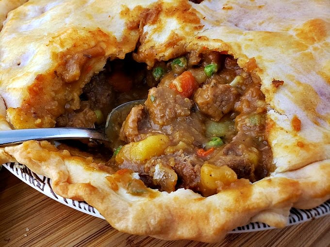 Close up image of a spoon digging into a rich and flavorful homemade beef pot pie.