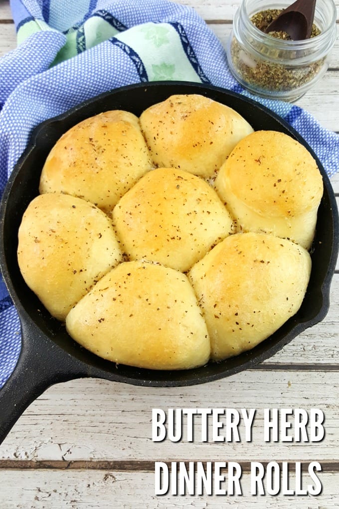 cast iron skillet with buttery dinner rolls next to a blue and green kitchen towel.