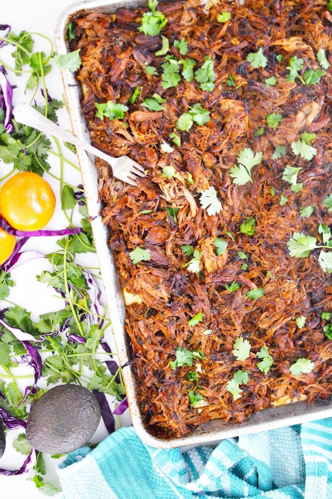 a sheet pan of crispy pork carnitas garnished with cilantro leaves