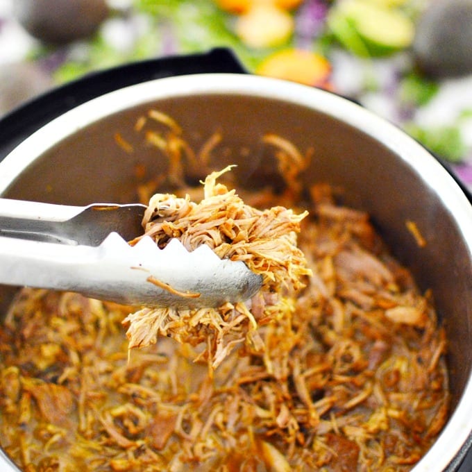 Tongs hold shredded pork canitas over an instant pot
