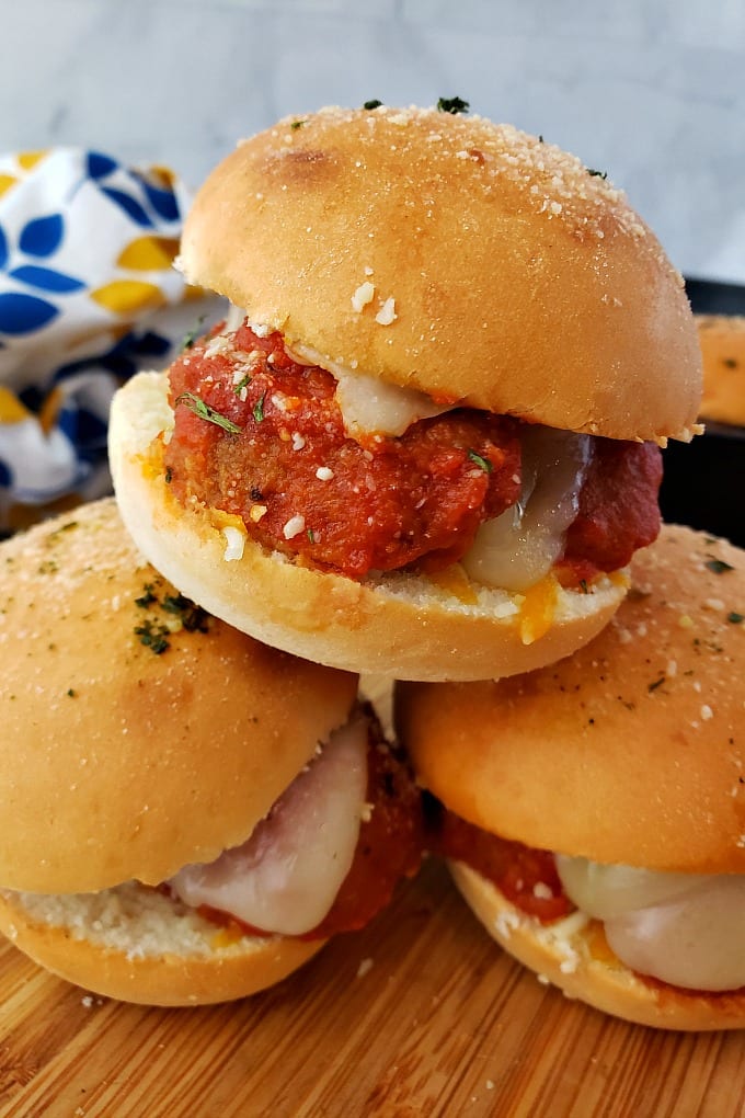 A stack of cheesy meatball sliders on a cutting board.