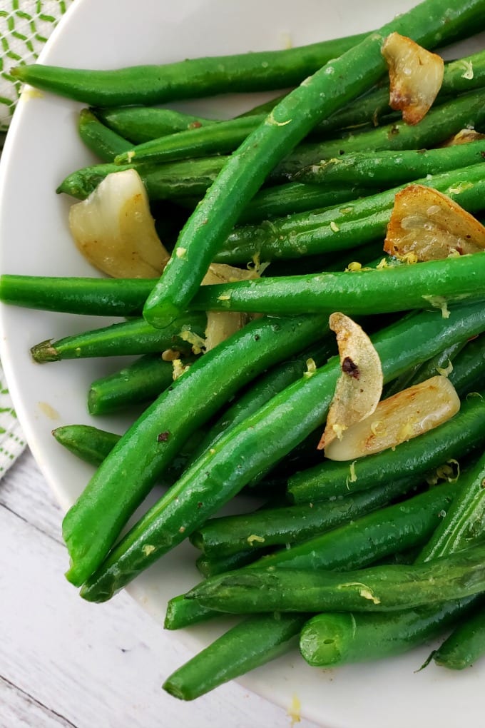 cooked and seasoned green beans in a white dish topped with sauteed garlic and lemon zest.