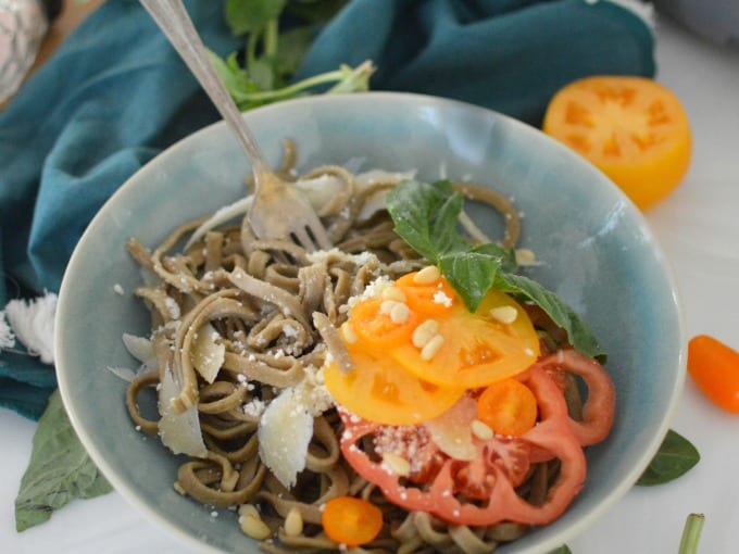 a bowl of cooked homemade spinach pasta with heirloom tomatoes and pine nuts