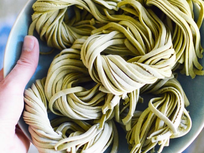 a hand holds swirls of homemade spinach pasta