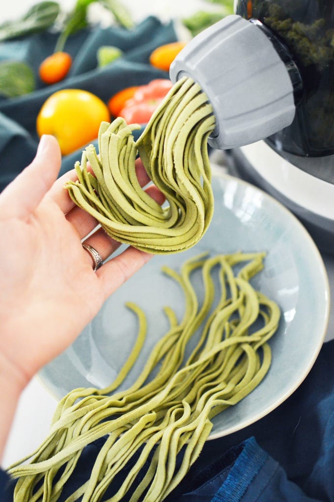 a hand catches the spinach pasta as it is extruded from a pasta maker