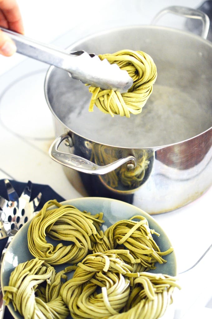 A pair of tongs holds a swirled bunch of homemade pasta over a pot of boiling water.