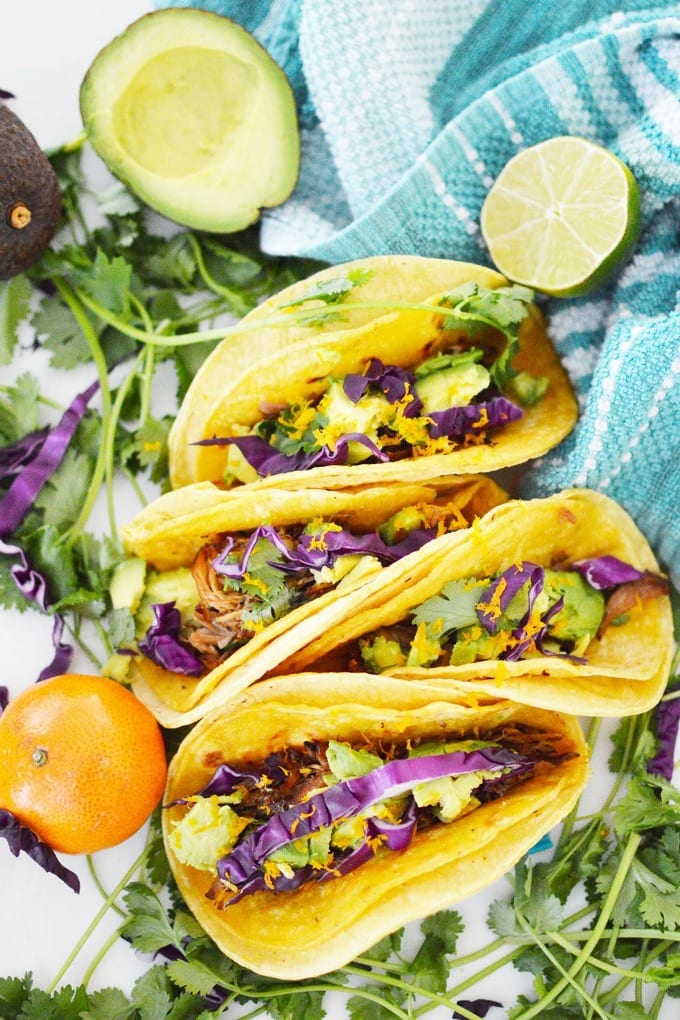 Instant Pot Pork Carnitas tucked into corn tortillas with avocado and purple cabbage.