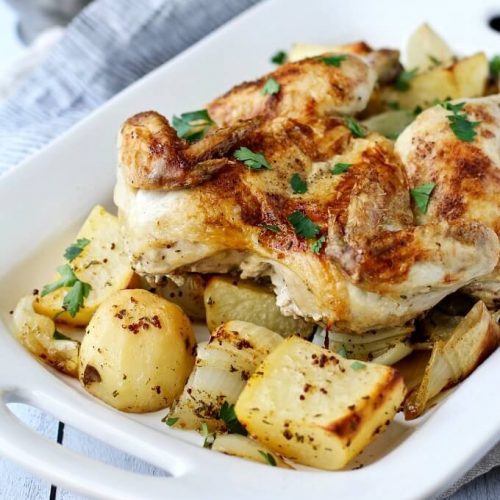 Sheet pan spatchcocked chicken with roasted potatoes in a white serving dish.