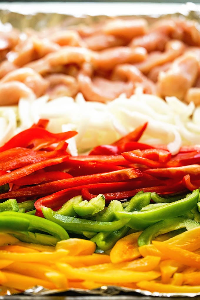 Peppers, onions, and chicken on a foil lined baking sheet.