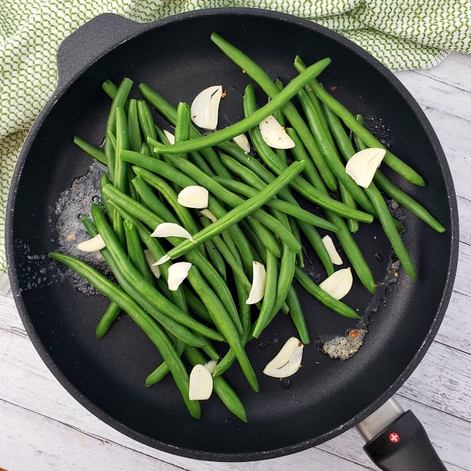 melted butter in a skillet with fresh seasoned green beans and sliced garlic 