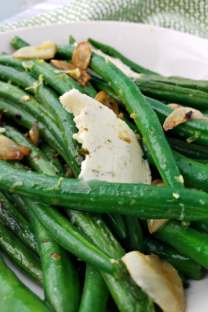 cooked and seasoned green beans in a skillet dish topped with sauteed garlic and compound butter