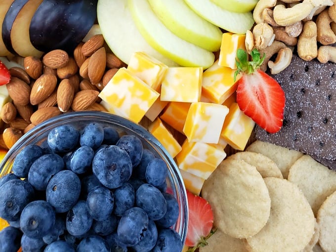 close up of a fruit and cheese platter including blueberries, colby jack cheese, crackers and nuts.