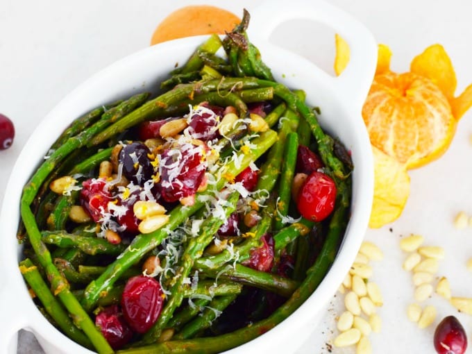 A white serving dish of asparagus with toasted pine nuts, fresh cranberries and Parmesan cheese.