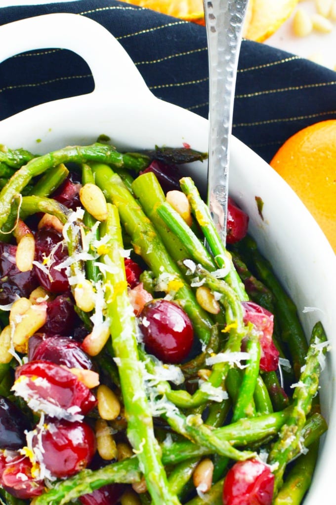 A white serving dish of pan seared asparagus with toasted pine nuts, fresh cranberries and Parmesan cheese