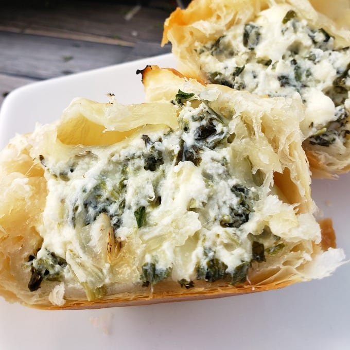 Golden brown Spinach Puff Pastry appetizer cut in half to reveal a cheese, chicken and spinach filling on a white serving tray.