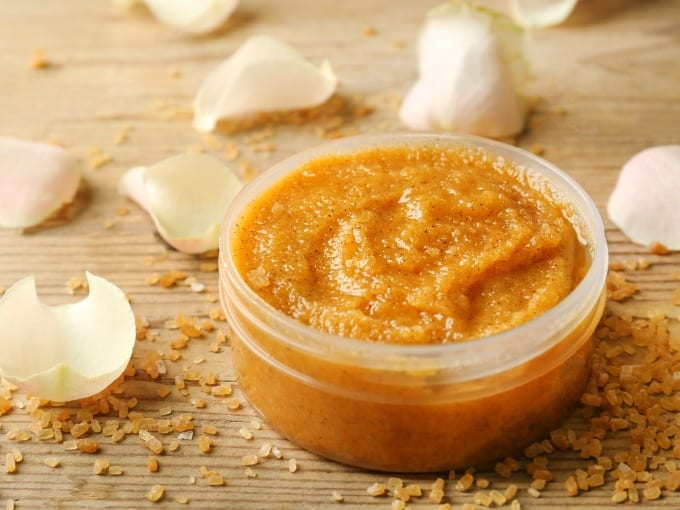 Body scrub, petals and sugar on wooden background