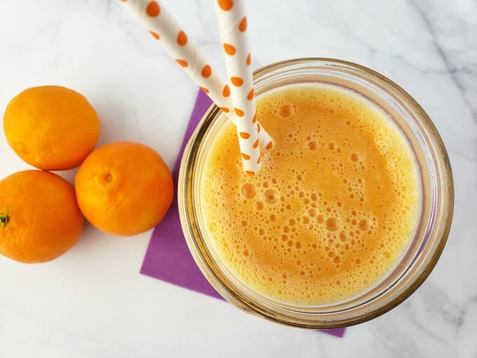 Top down view of a smoothie in a mason jar next to fresh clementines.