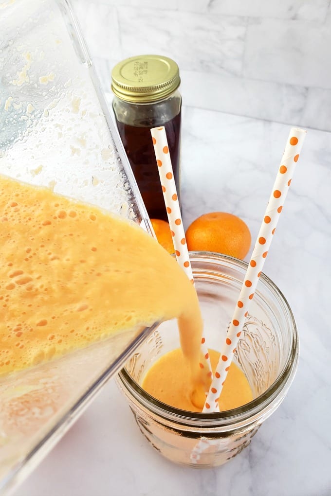 A clementine smoothie being poured from a blender into a mason jar 