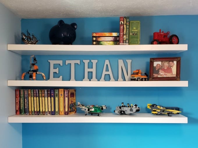 White DIY Floating Wood Shelves against a bright blue wall with books and toys.