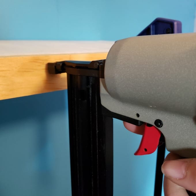 a hand holds a finish nailer attaching trim 