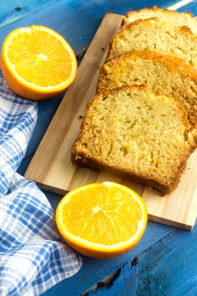 Orange Pound Cake Recipe - slices of orange pound cake on a cutting board near halved oranges and a blue and white kitchen towel