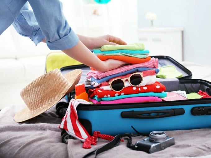 woman packing a suit case with clothes, hat, sunglasses and camera