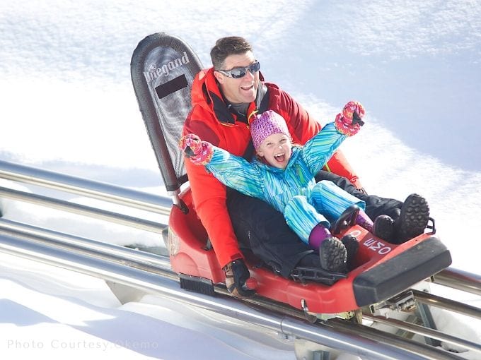 a dad and a little girl with their winter clothes on as they enjoy the thrill of ride on mountain coaster