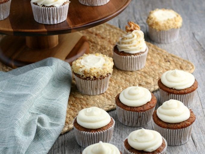 Carrot cupcakes with a cream cheese frosting topped with walnuts next to a blue cloth napkin.