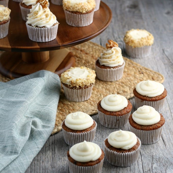 Carrot cupcakes with a cream cheese frosting topped with walnuts next to a blue cloth napkin.