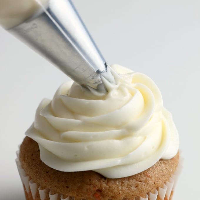 a piping bag fitted with a star tip adds the best cream cheese frosting recipe to the top of a cupcake.