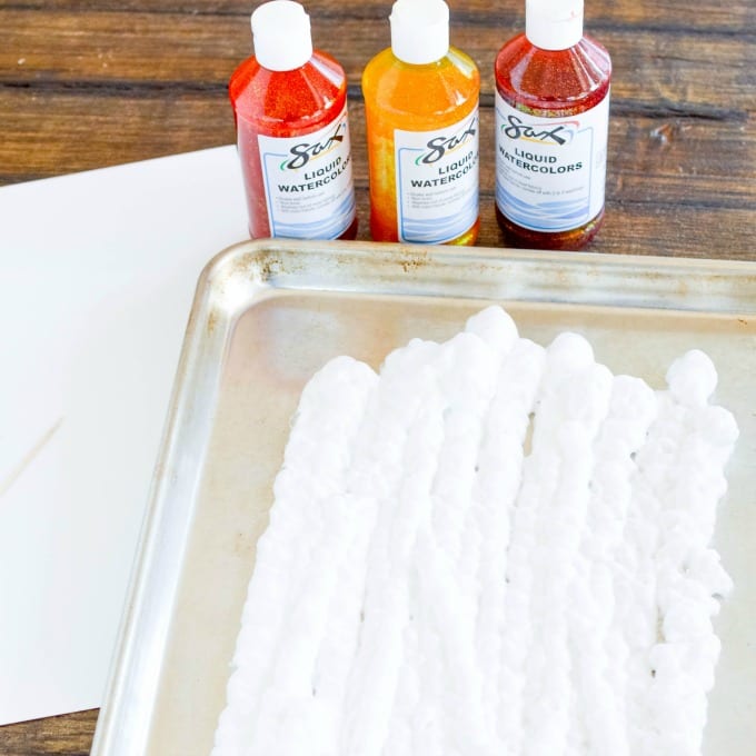 three bottles of paint and a baking sheet covered with shaving cream used for shaving cream painting project