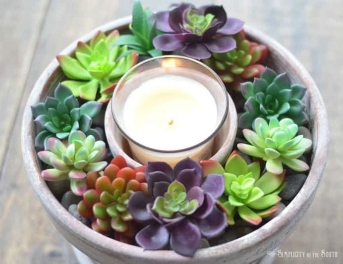 a bowl of faux succulents with a candle in the middle
