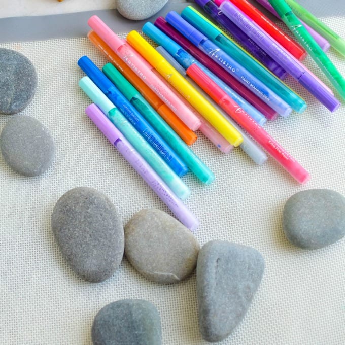 Smooth gray rocks with paint pens on a silicone mat.