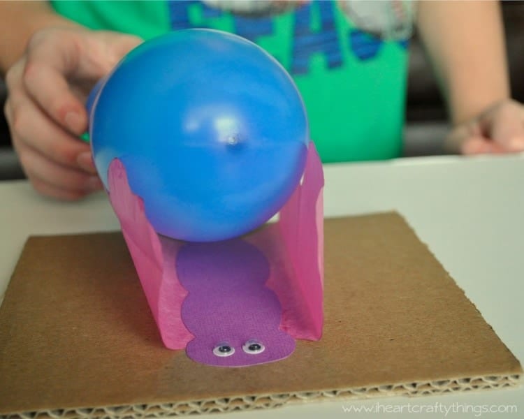 A piece of cardbord with a tissue paper butterfly holding a balloon.