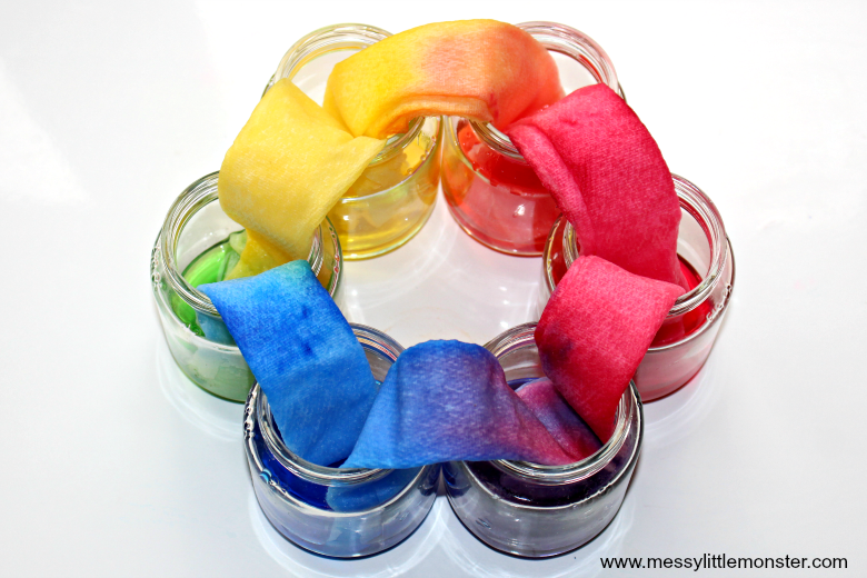 Top down image of colored water in glass jars traveling from one to another via paper towels.