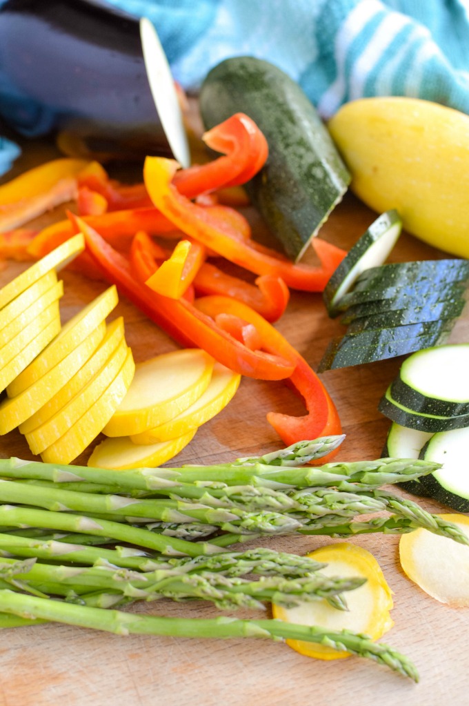 Raw zucchini, squash, bell peppers and asparagus on a cutting board.