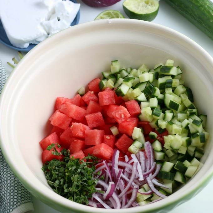 Mixing bowl filled with the ingredients for watermelon salad - watermelon, cucumber, mint, and red onion.