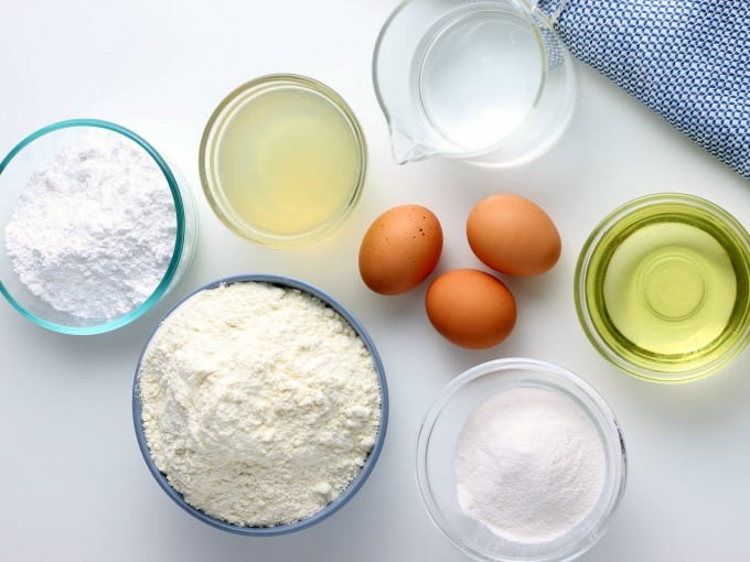 Ingredients for How to Make Lemon Cake including bowls of cake mix, lemon juice, water, oil and powdered sugar as well as three brown eggs.