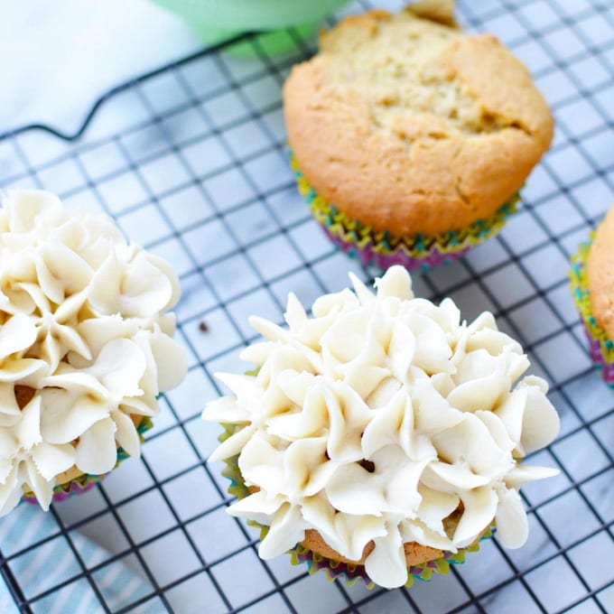 Vanilla cupcakes on a cooling rack. Some are frosted. Some are not.