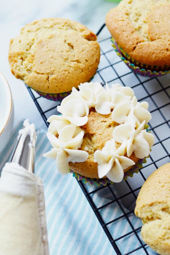 Vanilla cupcakes being frosted with a star piping tip.