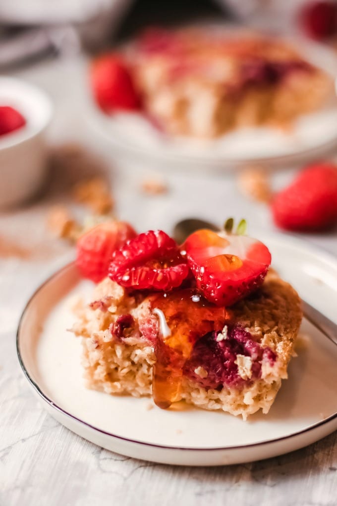 Baked oatmeal topped with fresh strawberries and maple syrup on a small white plate.